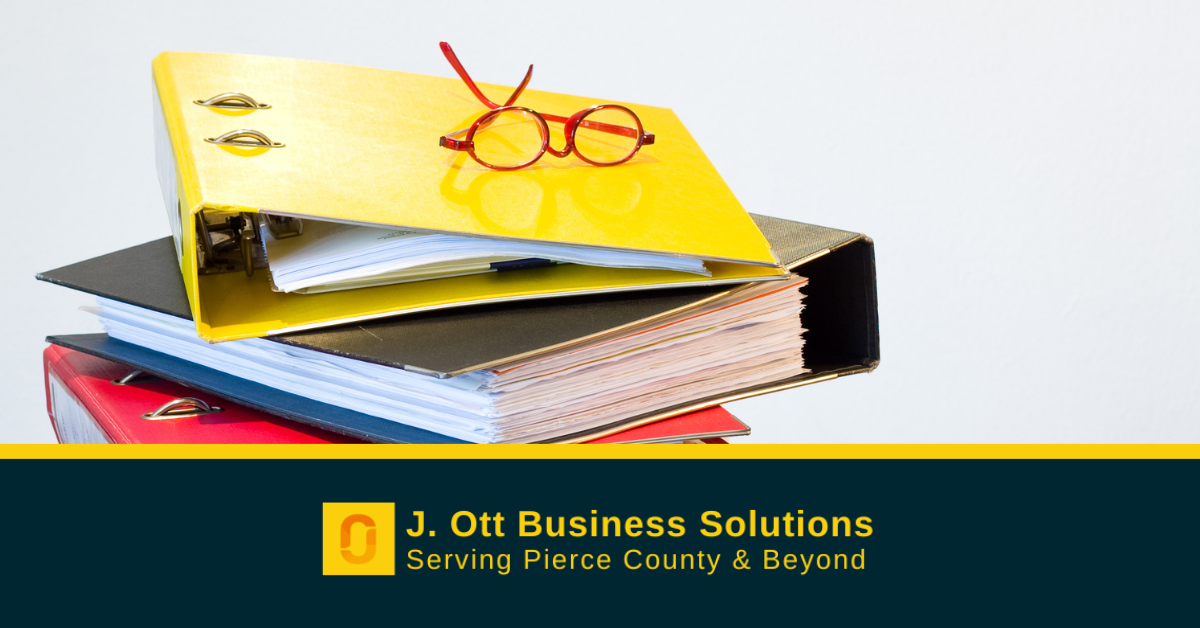 A pile of binders and ledgers with a pair of red reading glasses on top.